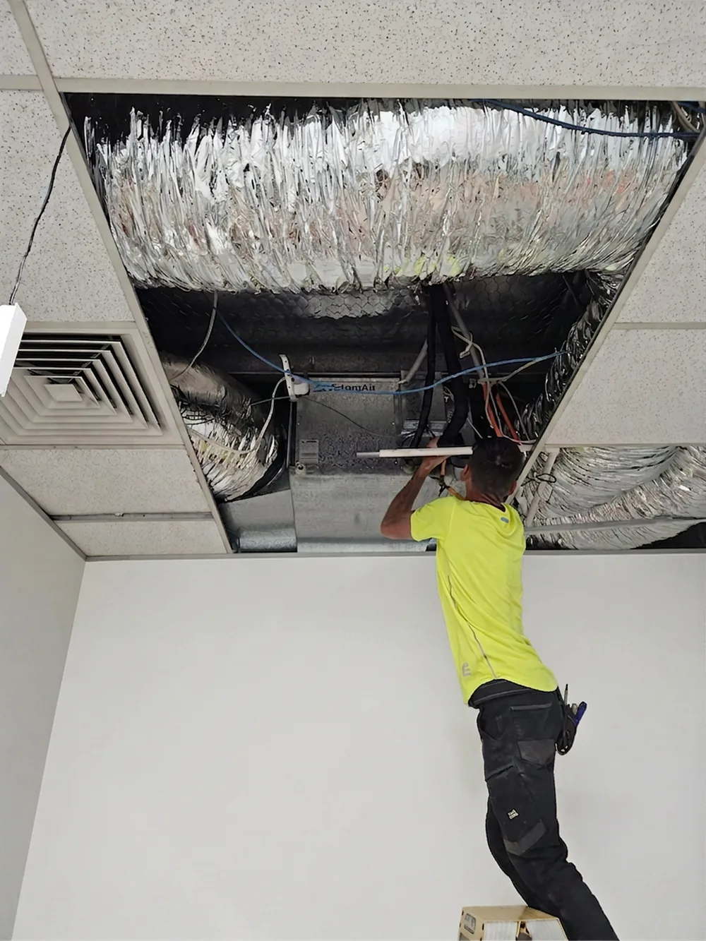 Technician servicing ducted air conditioning in a commercial ceiling